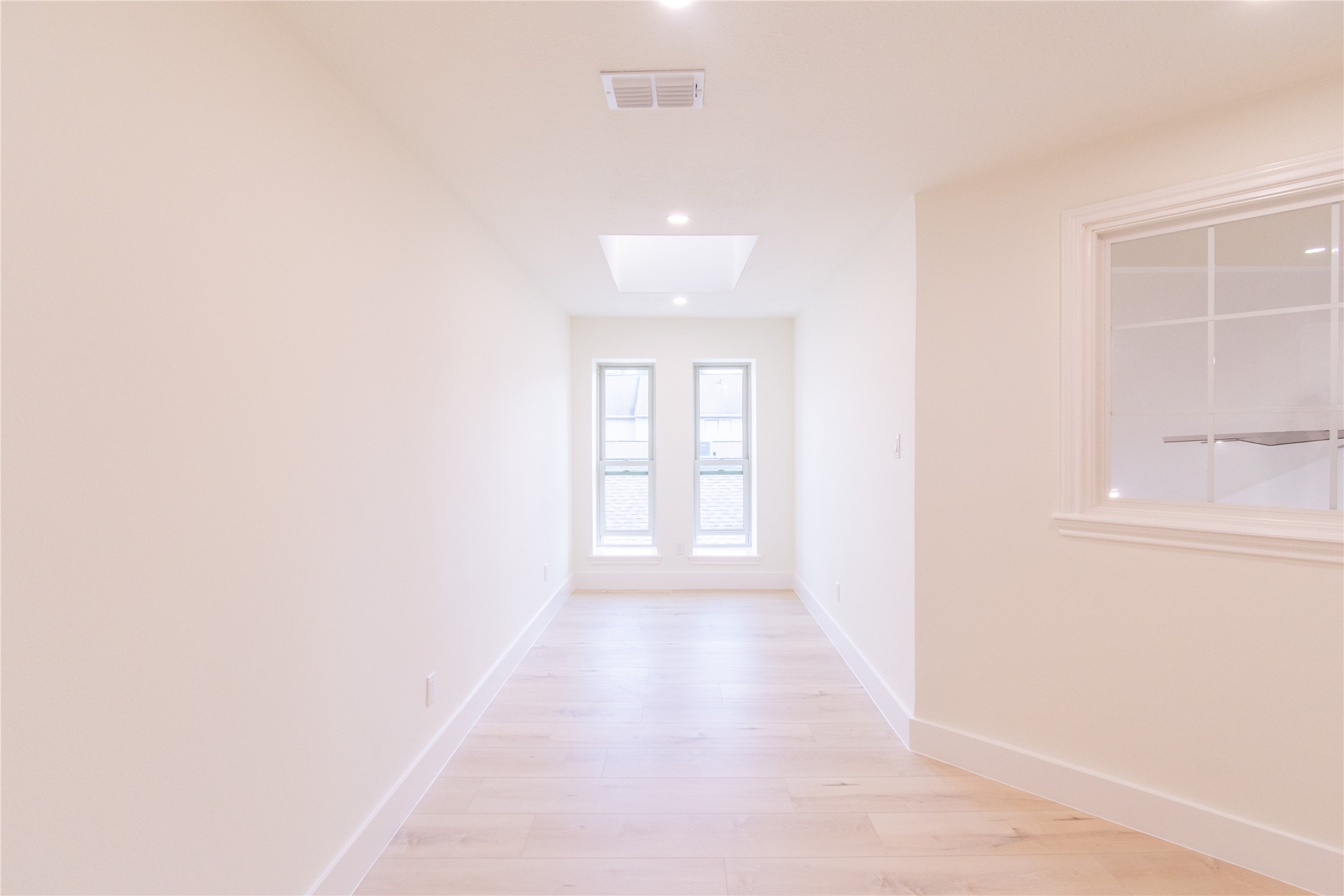 727 Bunker Hill Road, Unit 43 Houston, TX 77024 - Photo 27 of 34 Bright, narrow room with light wood flooring, featuring two tall windows at the end and a skylight above. A side window opens into an adjacent space, enhancing natural light flow.