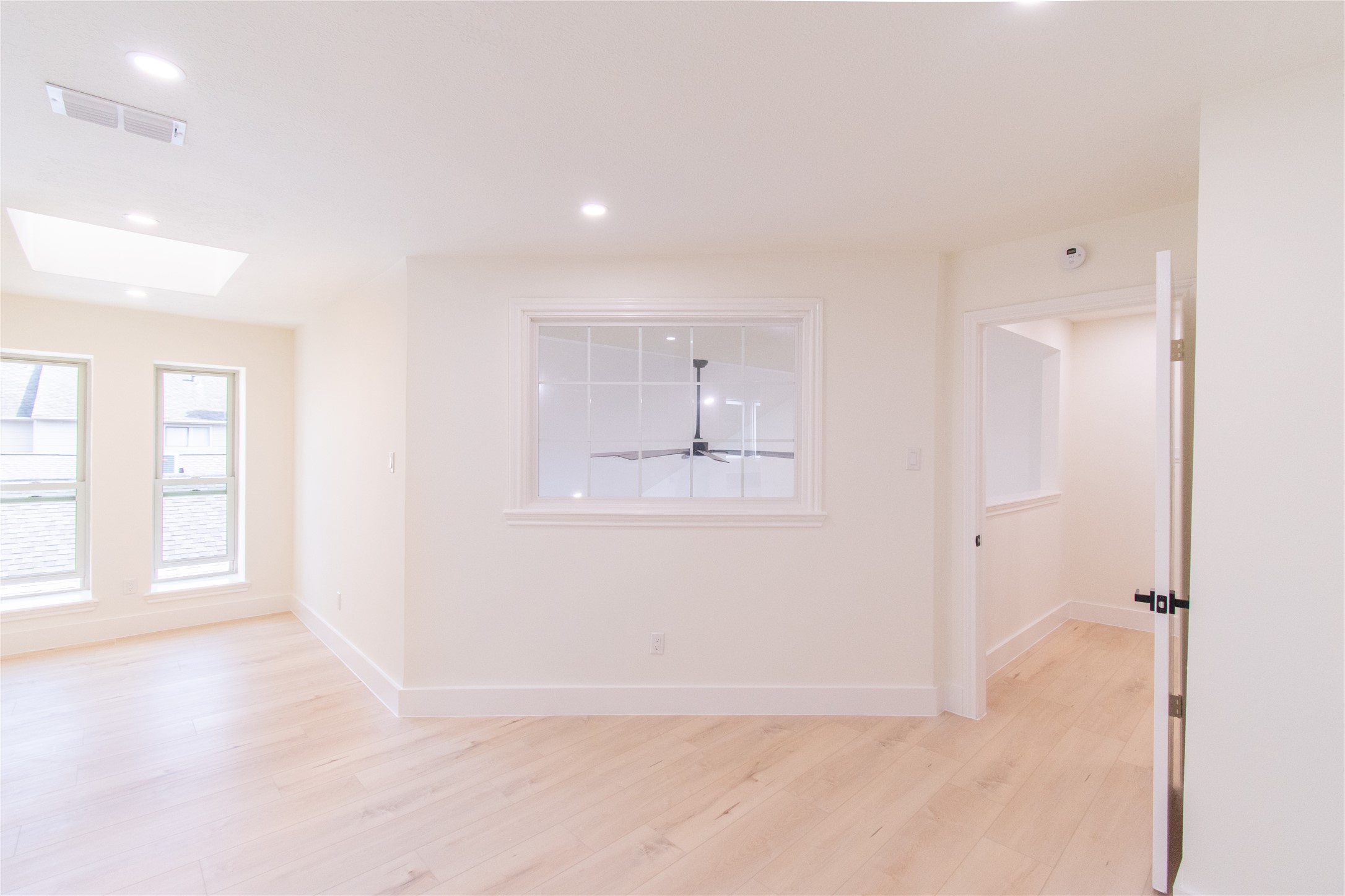 727 Bunker Hill Road, Unit 43 Houston, TX 77024 - Photo 28 of 34 Bright room with light wood flooring, recessed lighting, and two large windows. A skylight adds natural light. There's an interior window and a partially open door leading to another space.