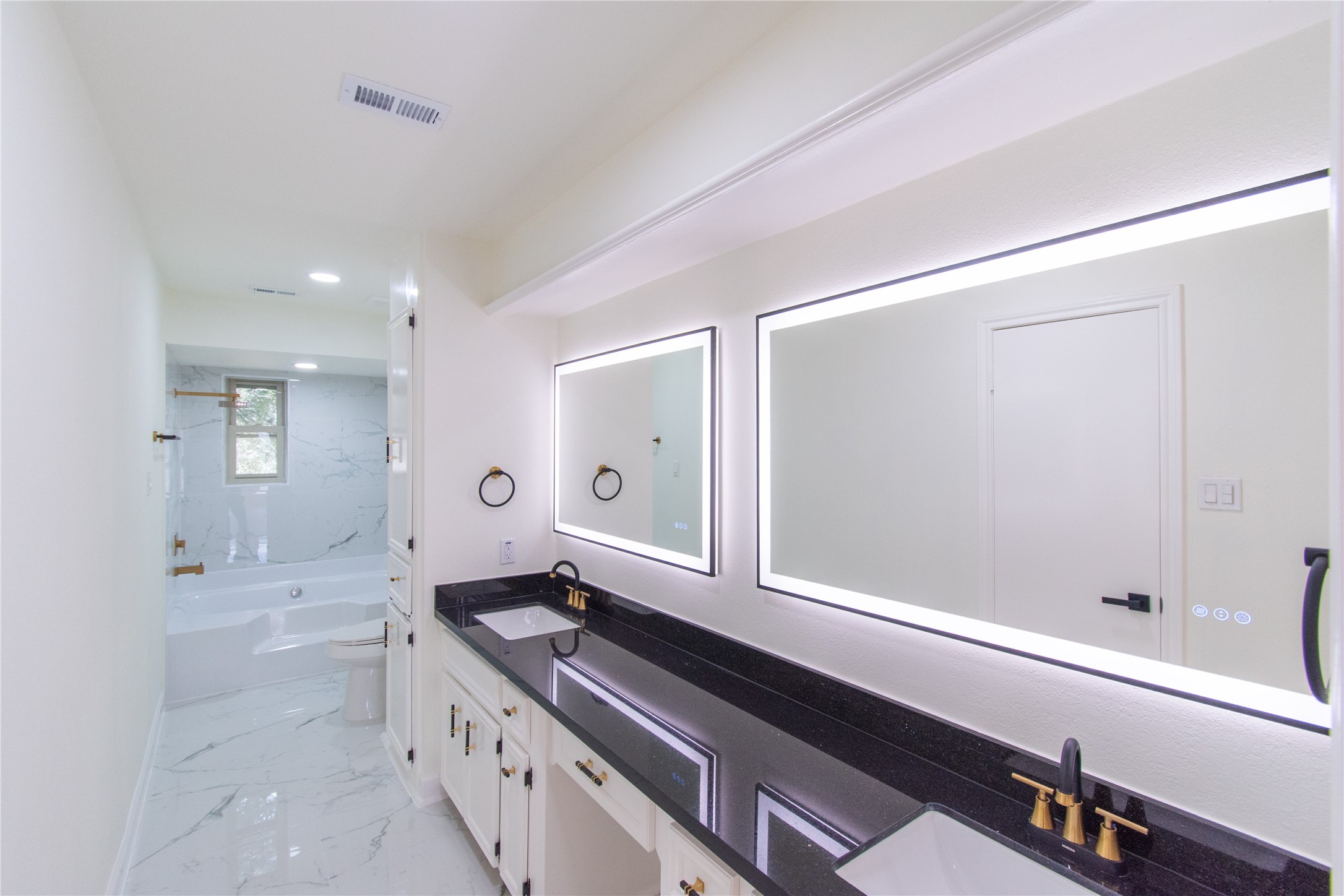 727 Bunker Hill Road, Unit 43 Houston, TX 77024 - Photo 29 of 34 Bathroom featuring a sleek double sink with countertops and gold fixtures. It has a large backlit mirror and a spacious bathtub with a marble-style surround. The room is bright and contemporary, offering a luxurious feel.