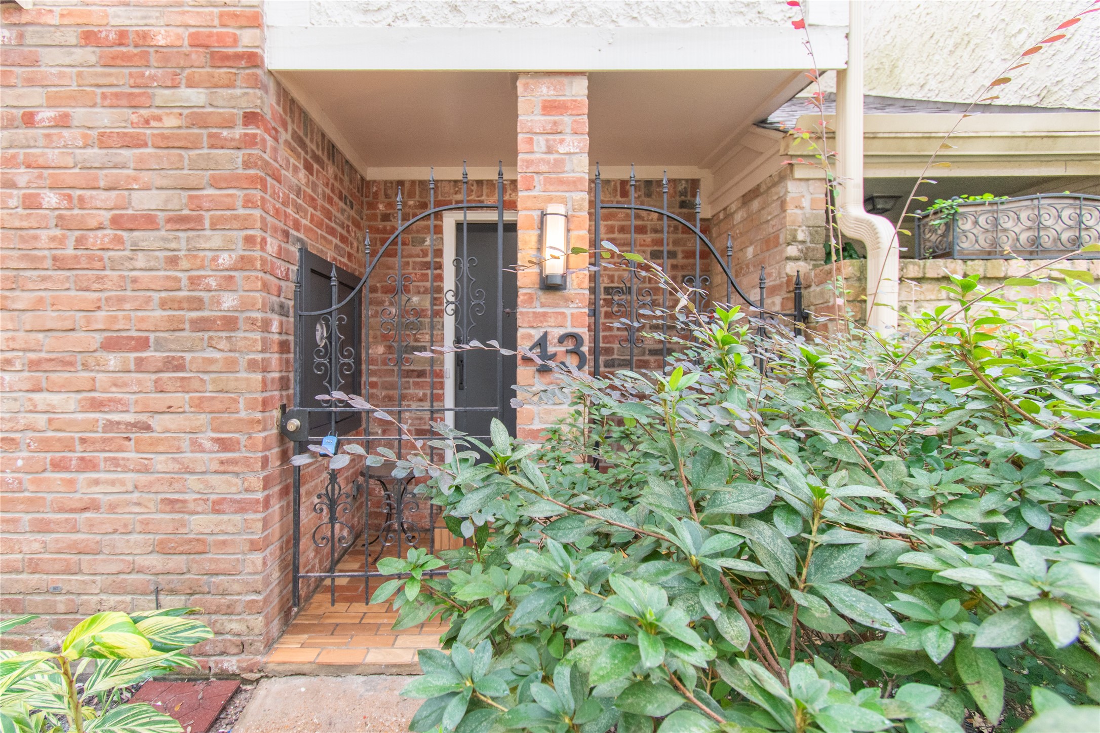 727 Bunker Hill Road, Unit 43 Houston, TX 77024 - Photo 3 of 34 Charming brick entryway with wrought iron gate, surrounded by lush greenery for added privacy and appeal.