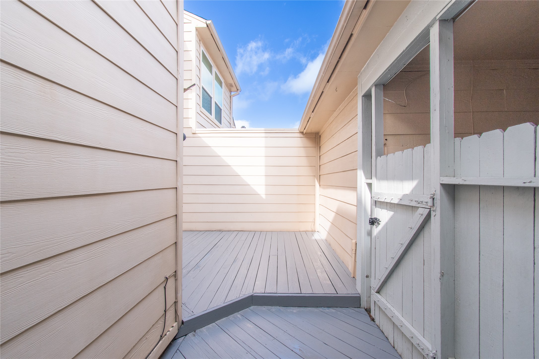 727 Bunker Hill Road, Unit 43 Houston, TX 77024 - Photo 32 of 34 Enclosed outdoor patio area with decking. It features a gate and is surrounded by walls, providing a private and cozy space, with a view of a neighboring building and a clear blue sky above.