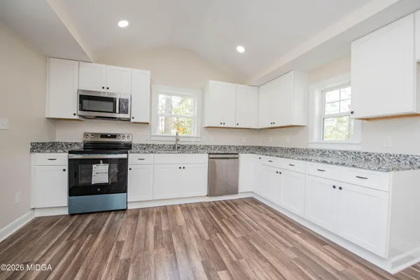 a kitchen with granite countertop a stove top oven a sink dishwasher a refrigerator and white cabinets with wooden floor