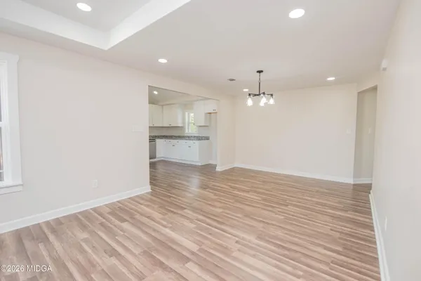 a view of empty room with wooden floor and kitchen
