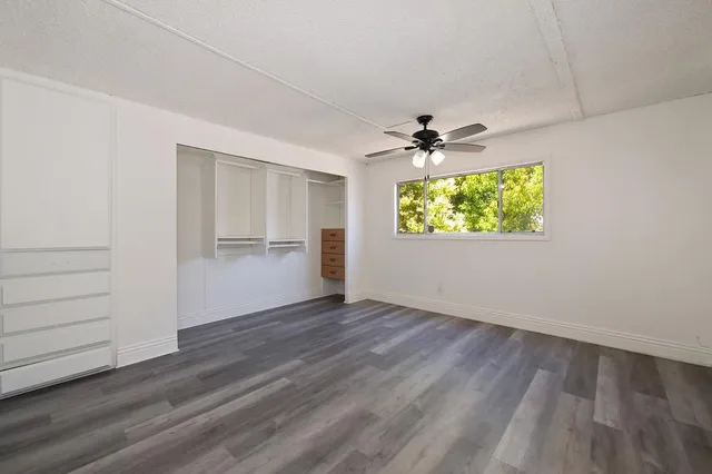 an empty room with wooden floor a ceiling fan and windows