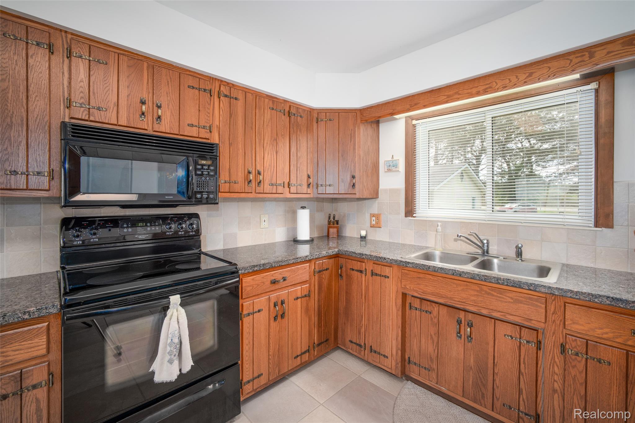 6240 Lakeshore Road Palms, MI 48465 - Photo 10 of 38 Kitchen with black appliances, wood finish cabinetry, dark countertops, tasteful backsplash, and light tile patterned floors