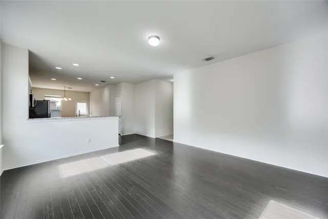 a view of an empty room with wooden floor and kitchen