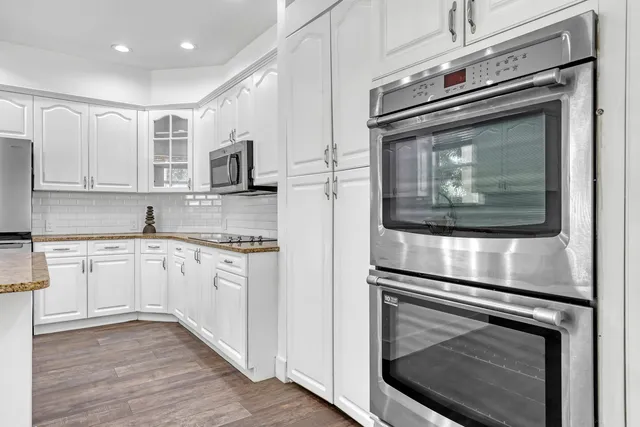 a kitchen with granite countertop white cabinets stainless steel appliances and wooden floor