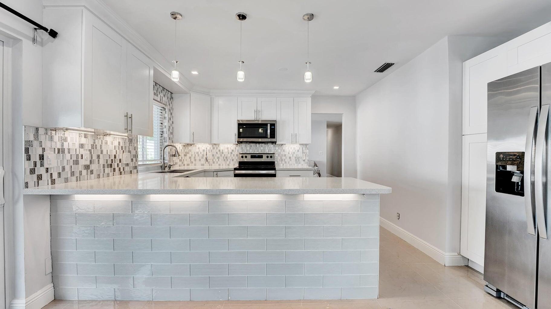 2941 Angler Drive Delray Beach, FL 33445 - Photo 17 of 34 a view of a kitchen with kitchen island a counter top space cabinets and stainless steel appliances