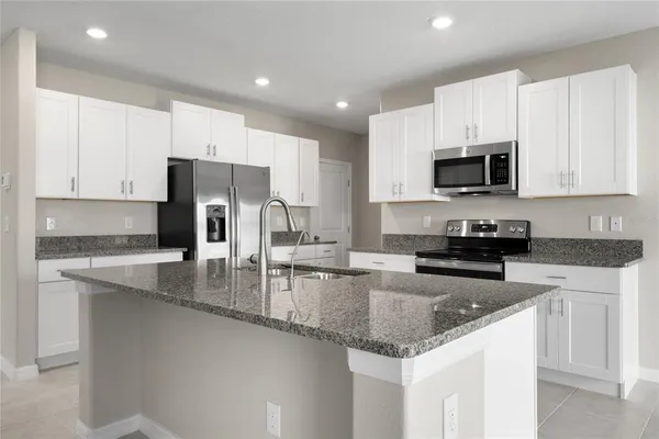a kitchen with stainless steel appliances granite countertop a stove a sink a microwave a refrigerator and white cabinets