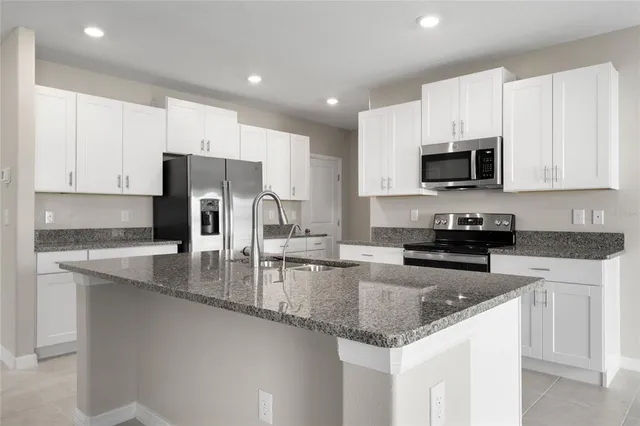 a kitchen with stainless steel appliances granite countertop a stove a sink a microwave a refrigerator and white cabinets