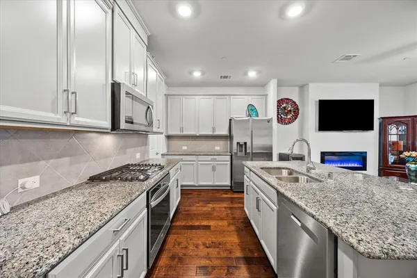 a large kitchen with stainless steel appliances granite countertop a stove top oven a sink dishwasher and a microwave with wooden floor