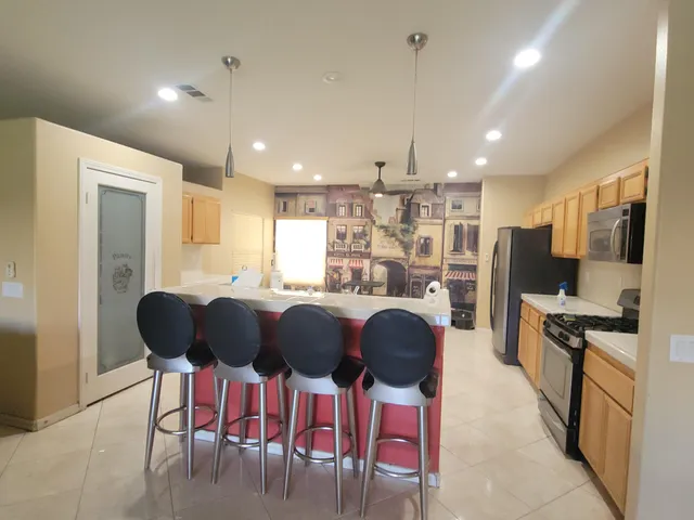 a kitchen with stainless steel appliances kitchen island granite countertop a refrigerator a stove a sink a dining table and chairs with wooden floor