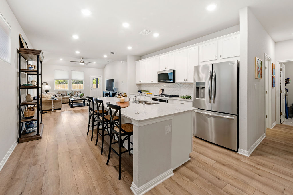 2417 Roosevelt Road Leander, TX 78641 - Photo 13 of 40 Kitchen featuring appliances with stainless steel finishes, a kitchen island with sink, white cabinetry, a kitchen bar, and tasteful backsplash