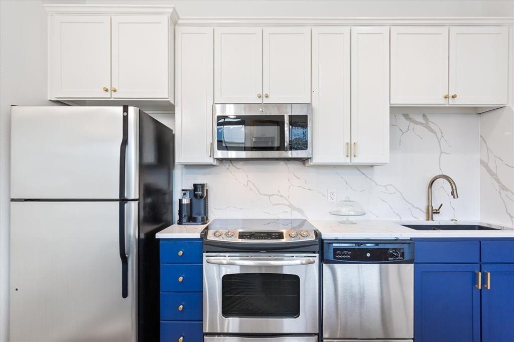 330 Austin Avenue, Unit 318 Waco, TX 76701 - Photo 17 of 22 Kitchen featuring appliances with stainless steel finishes, white cabinetry, decorative backsplash, blue cabinets, and light stone counters