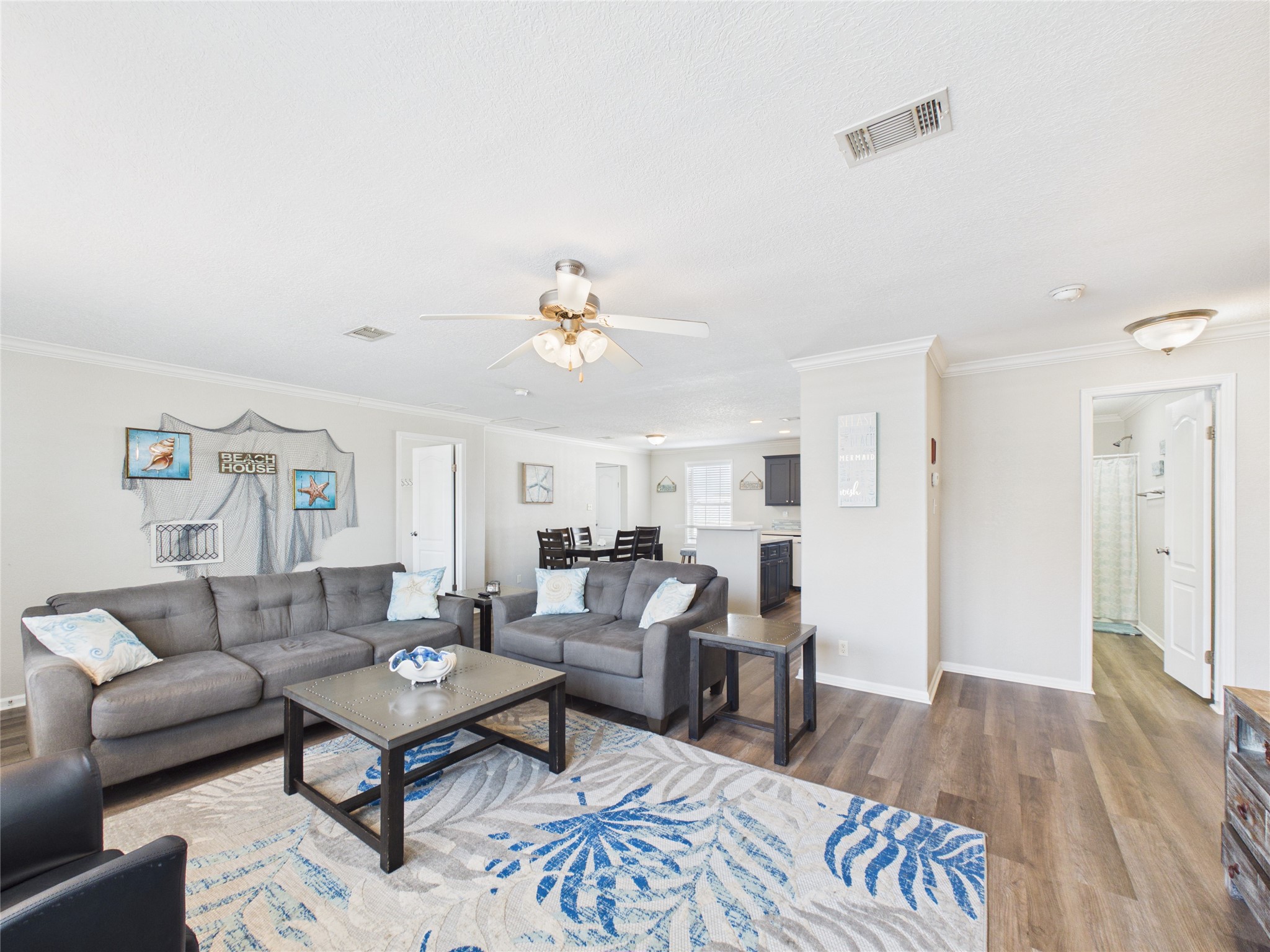 905 Meynig Drive Crystal Beach, TX 77650 - Photo 12 of 50 This photo features a spacious, open-concept living area with modern furnishings and a light, neutral color palette. It includes a comfortable seating arrangement with two sofas, a ceiling fan, and a large area rug. The room is well-lit with ample natural light, and there's a seamless flow into the dining and kitchen areas.