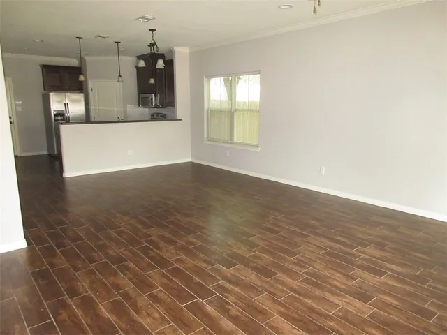 an empty room with wooden floor and kitchen view