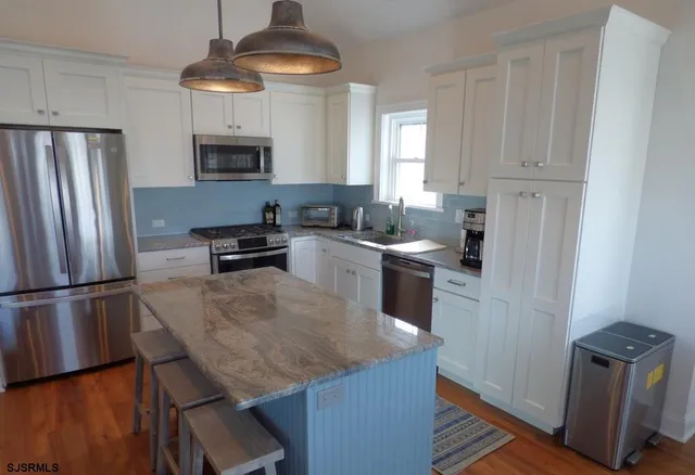 a kitchen with stainless steel appliances granite countertop a refrigerator a stove a sink dishwasher and white cabinets with wooden floor