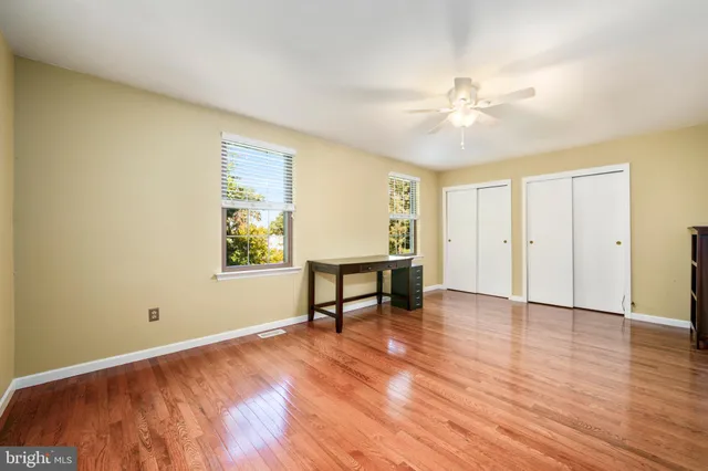 an empty room with wooden floor fan and windows