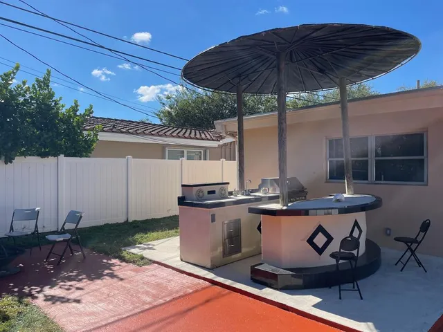 a view of a backyard with table and chairs under an umbrella with a barbeque