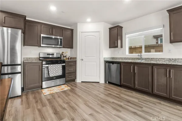 a kitchen with stainless steel appliances granite countertop a stove a sink dishwasher a refrigerator and a microwave oven with wooden floor