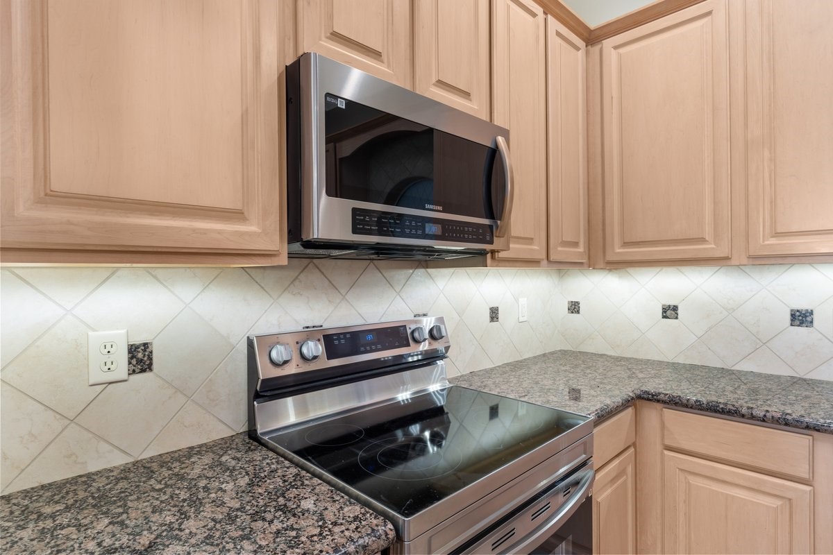 168 Lake Point Boulevard, Unit C102 Conroe, TX 77356 - Photo 7 of 35 This kitchen features modern stainless steel appliances, including a sleek stove and microwave, complemented by granite countertops and light wood cabinetry. The tiled backsplash adds a sophisticated touch.
