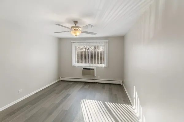 an empty room with wooden floor chandelier fan and windows