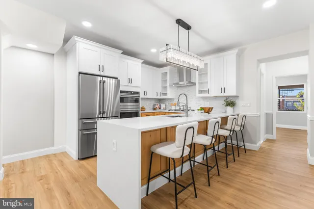 a large kitchen with kitchen island a sink a stove a refrigerator and white cabinets with wooden floor