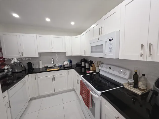 a kitchen with granite countertop a sink dishwasher stove and white cabinets