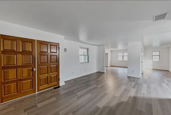 an empty room with wooden floor closet and windows