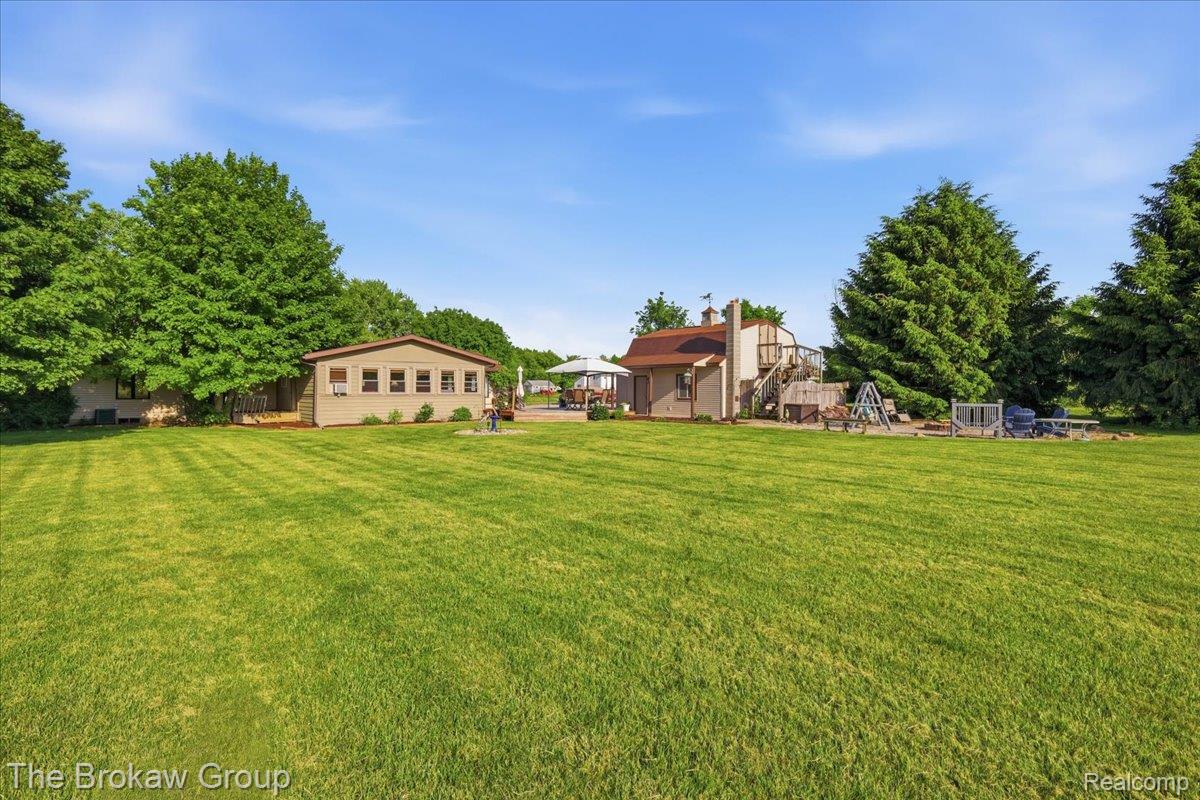 5461 North Henderson Road Davison, MI 48423 - Photo 58 of 64 Spacious rear yard with expansive lawn, mature perimeter trees, detached outbuilding with multiple windows, and a multi-level deck