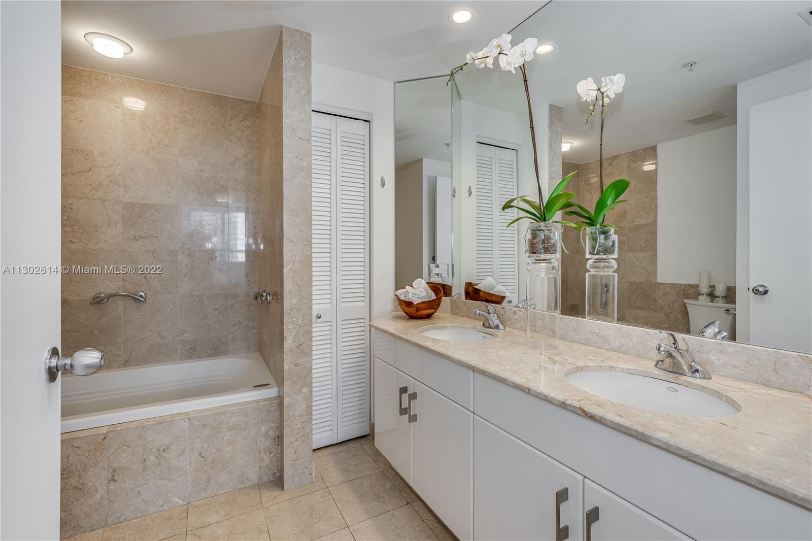 801 Brickell Key Boulevard, Unit 1701 Miami, FL 33131 - Photo 17 of 32 a bathroom with a granite countertop sink a mirror a bathtub and a shower