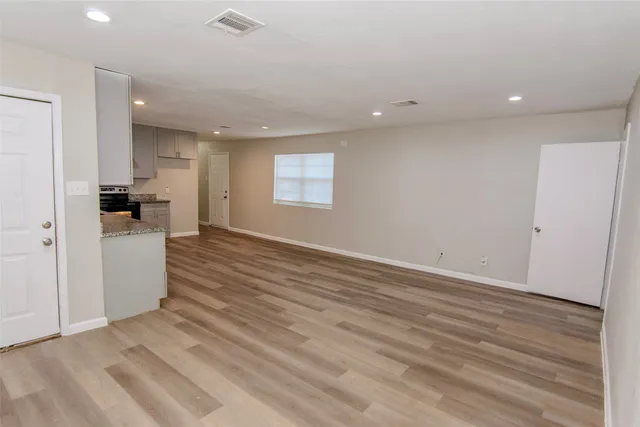 an empty room with wooden floor and a kitchen