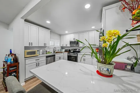 a kitchen with stainless steel appliances a white refrigerator a kitchen island a stove and a dining table with wooden floor