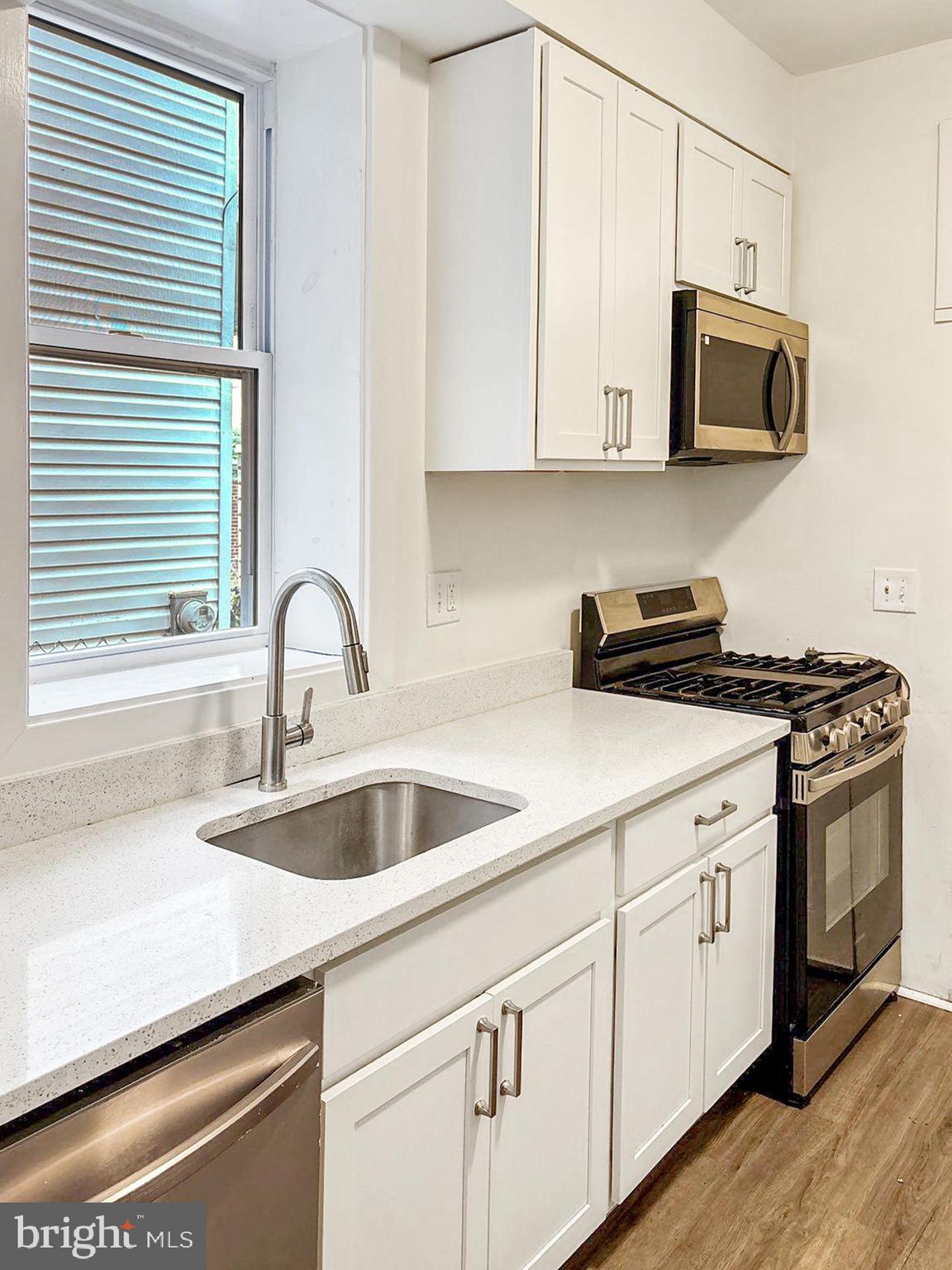 2217 Riggs Avenue Baltimore, MD 21216 - Photo 7 of 26 a kitchen with stainless steel appliances granite countertop a sink a stove and microwave with wooden floor