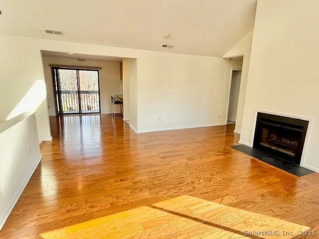 a view of an empty room with wooden floor and a fireplace