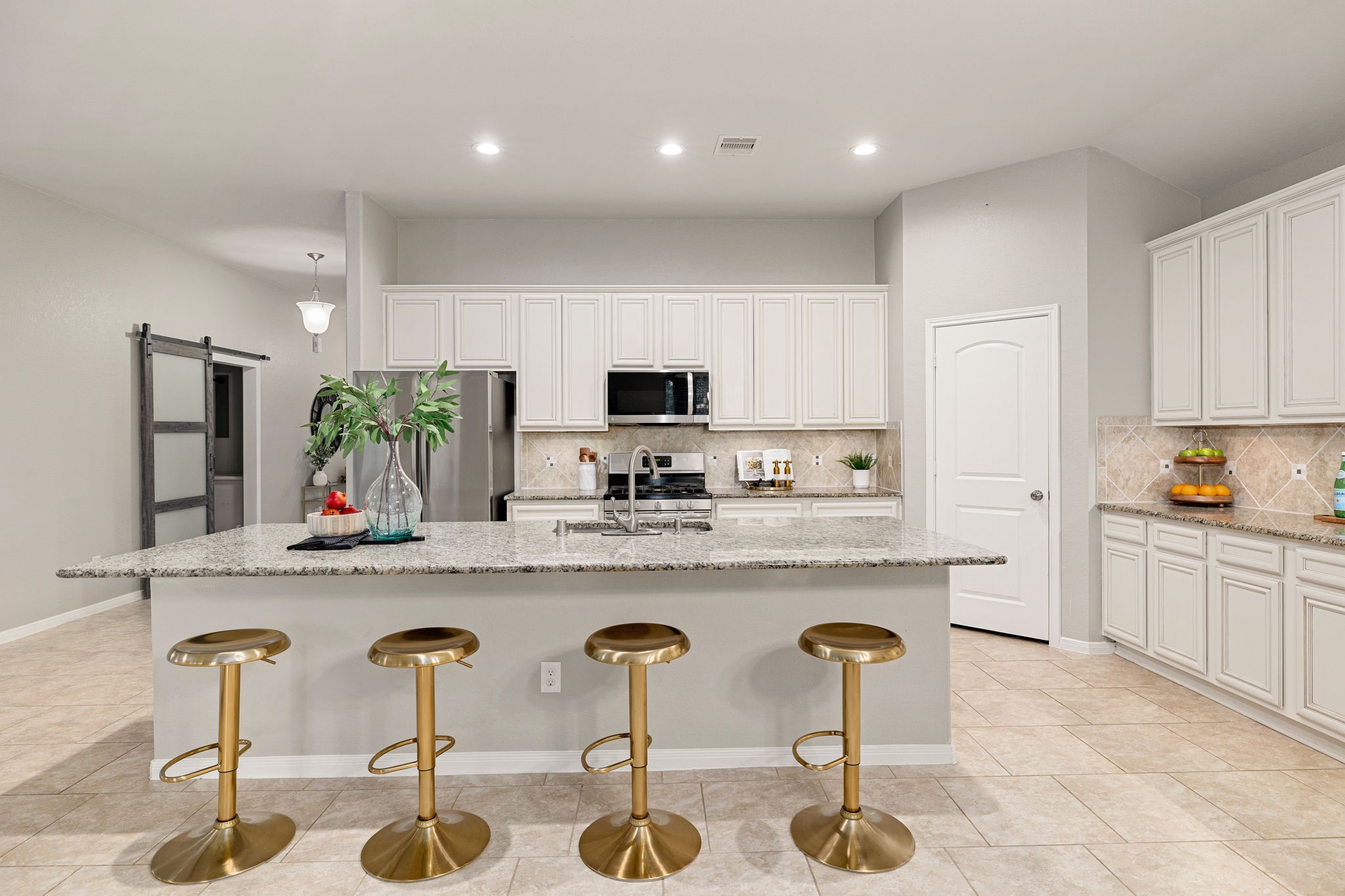 14023 Beaverhead Range Court Conroe, TX 77384 - Photo 8 of 30 This bright and expansive open-concept kitchen serves as the luminous heart of the home, perfectly designed for seamless hosting. High ceilings and a crisp white-on-white palette amplify the natural light, while polished floors provide an organic warmth that flows throughout the main living area. The massive central island offers a sleek, unobstructed surface that naturally bridges the culinary space with the surrounding rooms, creating an airy atmosphere ideal for gatherings.