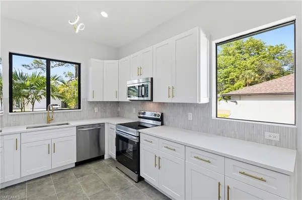 a kitchen with white cabinets appliances a sink and a window