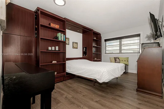 a bedroom with a bed and dresser with wooden floor