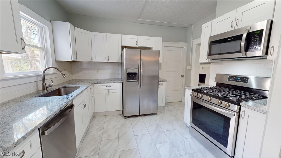 3174 Oak Road Cleveland, OH 44118 - Photo 12 of 33 Kitchen with stainless steel appliances, tasteful backsplash, light marble finish flooring, and white cabinets