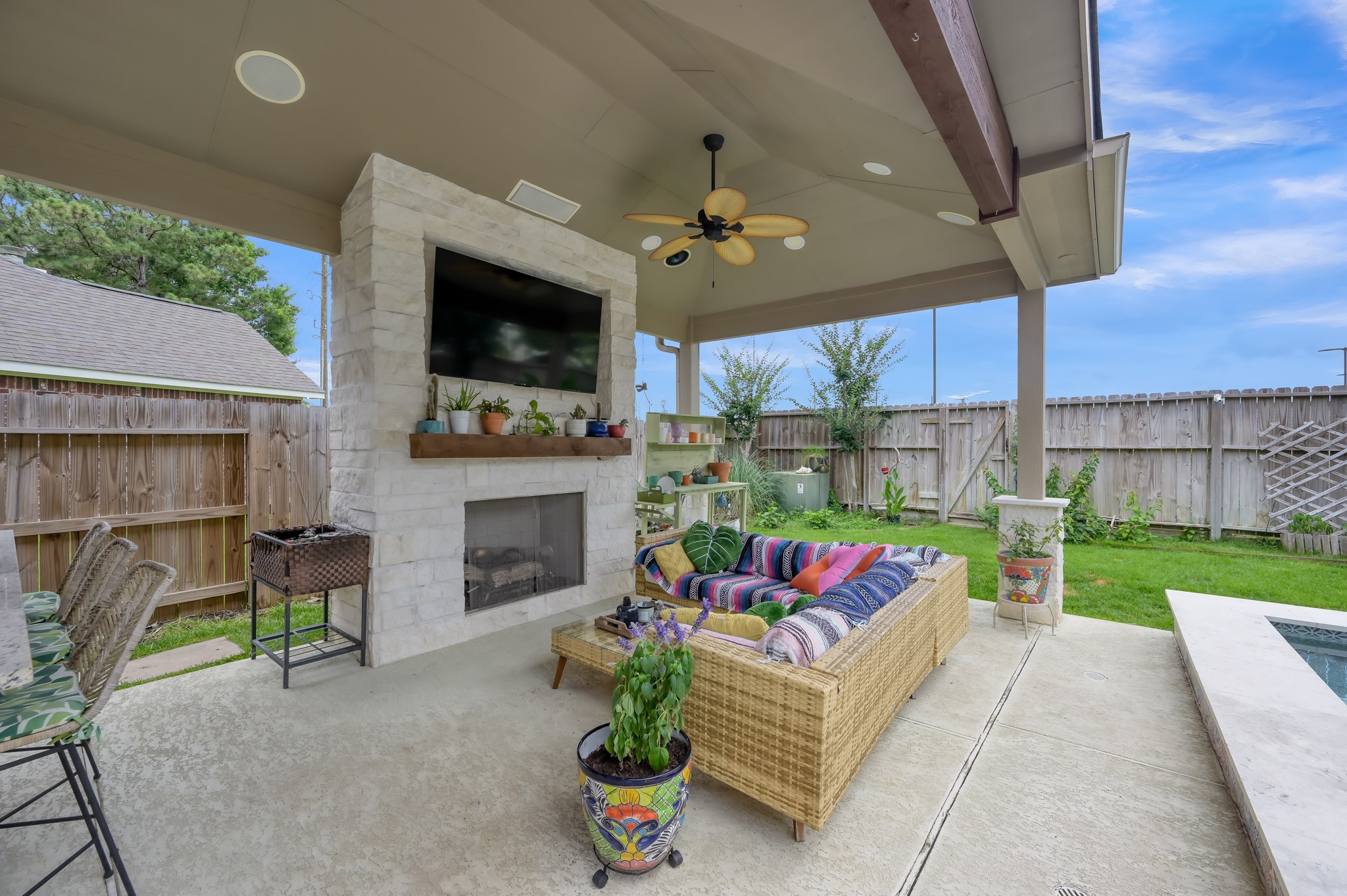28522 Misty Cliff Lane Spring, TX 77386 - Photo 10 of 12 Resort-style outdoor living area featuring a stone fireplace, mounted TV, and comfortable covered lounge space overlooking the pool. Perfect for relaxing or entertaining in every season.