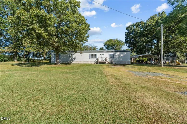 a view of a pool with lawn chairs and large trees