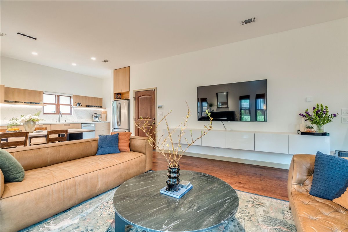 3012 South 4th Street, Unit B Austin, TX 78704 - Photo 6 of 40 Open-concept living area featuring rich wood-finish flooring, a contemporary floating media console, recessed lighting, and a well-appointed kitchen with light wood cabinetry and stainless steel appliances