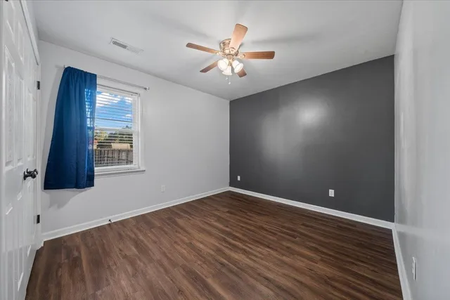 a view of an empty room with wooden floor and a ceiling fan
