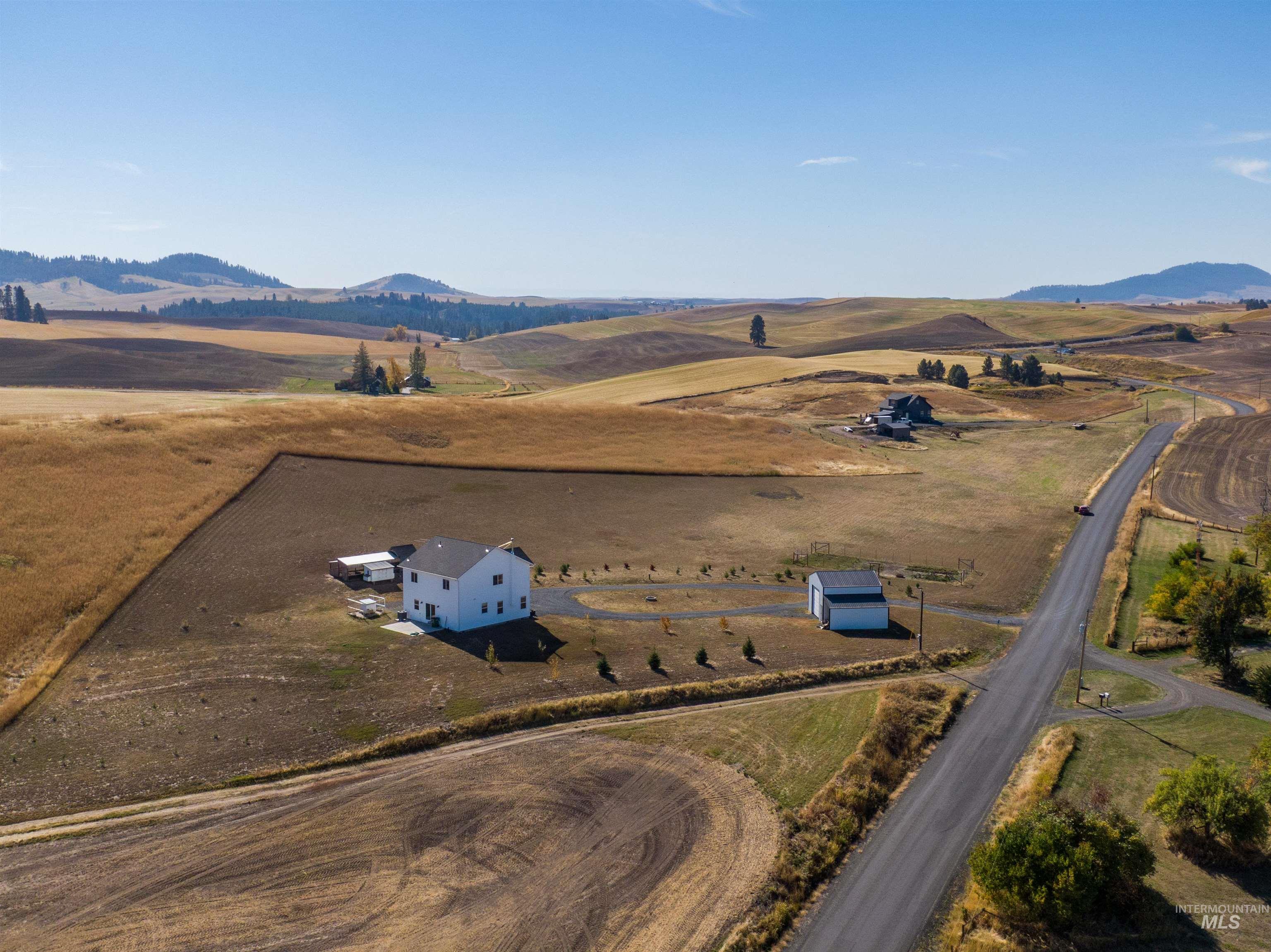 1032 Duffield Flat Road Potlatch, ID 83855 - Photo 50 of 50 Expansive property featuring a white residence with a dark roof, a detached auxiliary building, and a paved driveway, set amidst rolling hills and agricultural fields
