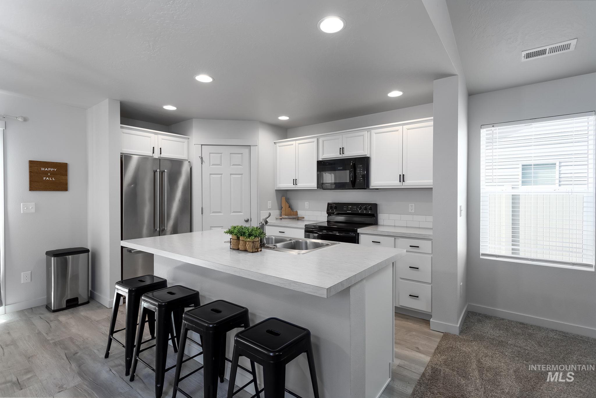 12771 Carkhill Street Caldwell, ID 83607 - Photo 7 of 13 Kitchen featuring white cabinetry, a large center island with a light-toned countertop, stainless steel refrigerator, and black appliances
