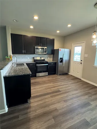a large kitchen with stainless steel appliances granite countertop a stove a refrigerator a sink a microwave and with wooden cabinets