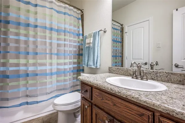 a bathroom with a granite countertop sink a toilet a mirror and shower curtain