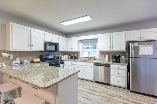 a kitchen with stainless steel appliances granite countertop a stove top oven a sink a refrigerator and white cabinets