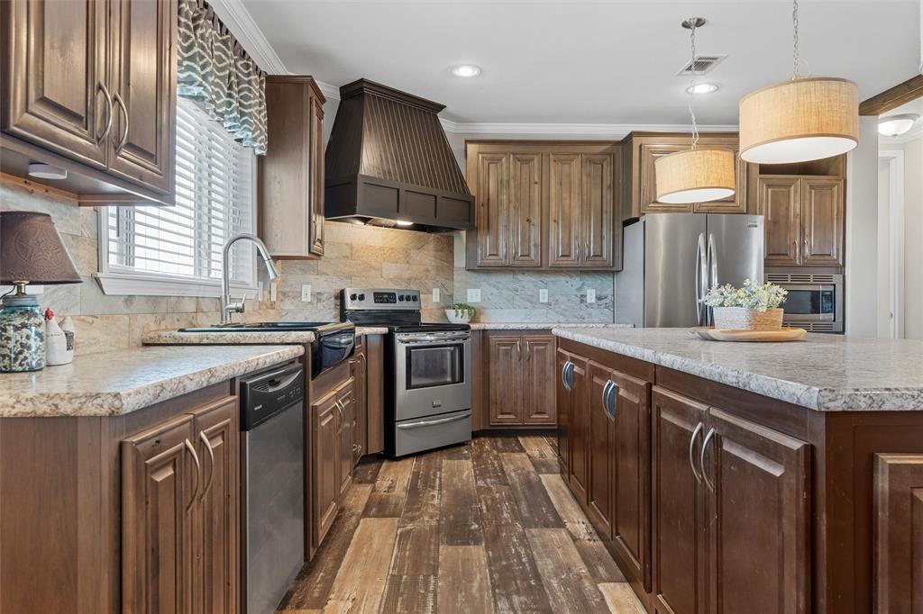 3449 Bluhm Road West, TX 76691 - Photo 13 of 40 Kitchen featuring custom range hood, appliances with stainless steel finishes, backsplash, dark wood-style flooring, and hanging light fixtures