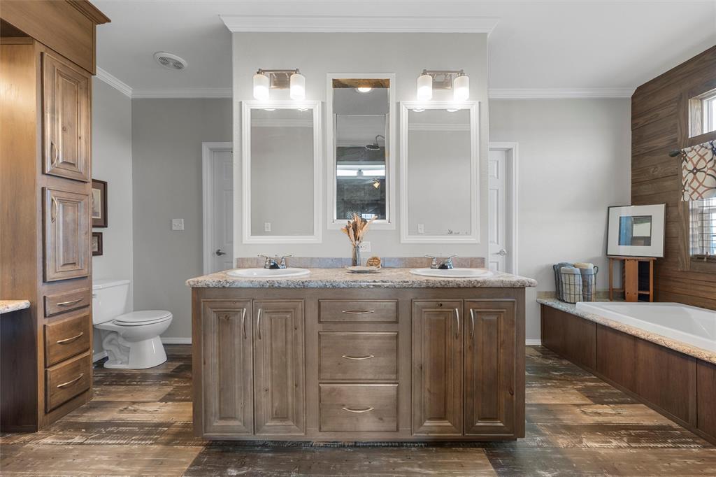 3449 Bluhm Road West, TX 76691 - Photo 19 of 40 Full bathroom with double vanity, dark wood-style floors, a garden tub, ornamental molding, and wooden walls
